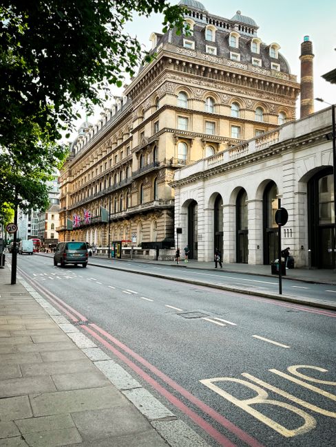 A city street scene outside a multi-story historic building with ornate architectural details, including arched windows and decorative cornices, situated on a corner with a white stone facade. The str